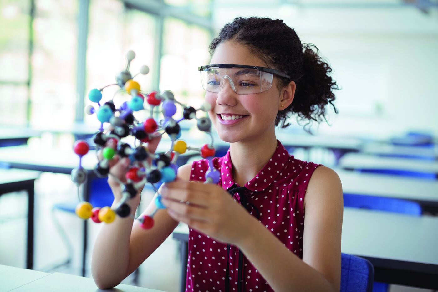 Schülerin mit Schutzbrille hält ein Molekülmodell