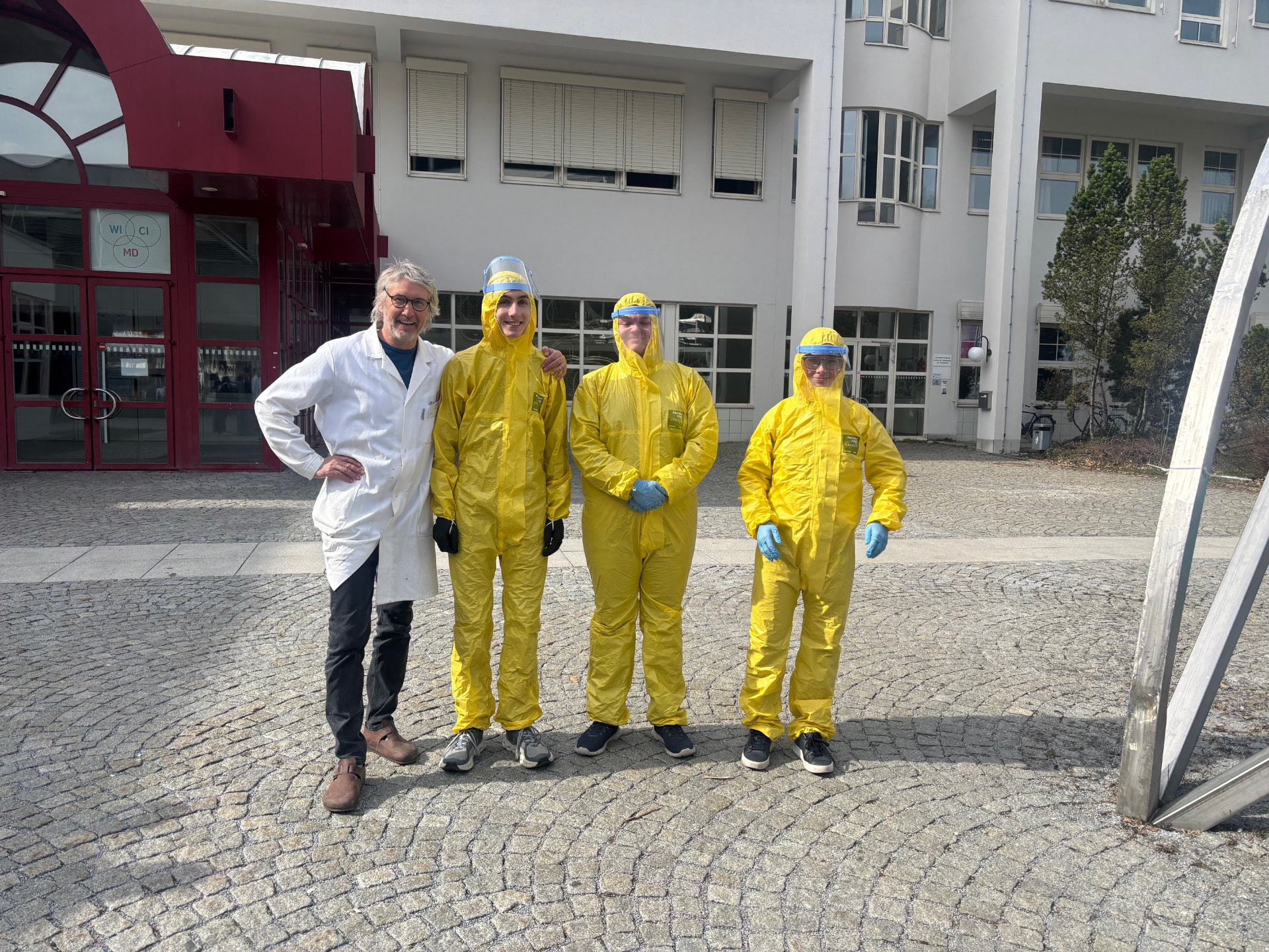 Workshop-Gruppe vor dem Gebäude in Laborkittel und Schutzanzügen