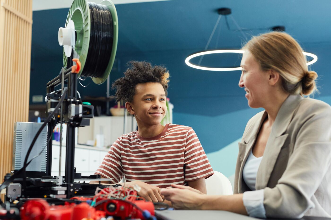Jugendlicher und Betreuerin vor einem 3D-Drucker